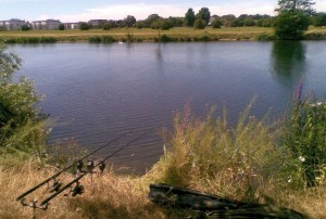 Two carp rods on the River Thames at Chertsey Mead, viewed on a hot sunny day. Dumsey Meadow is present in the background.