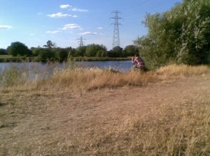 An angler fishes the Thames at Chertsey Meads on a hot summer day.