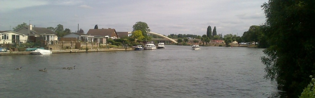 Looking across the Thames at Walton on a summer day, with a boat moving up the river.